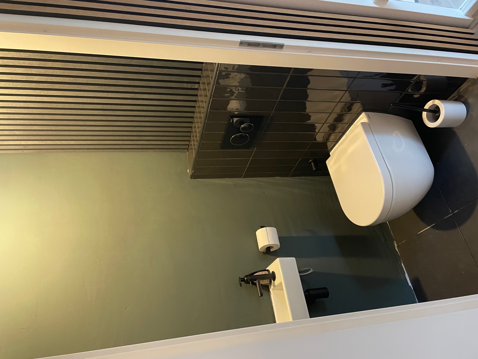 Afgewerkte toiletruimte met zwart tegelwerk, hangtoilet en compacte fontein na renovatie in Hoofddorp